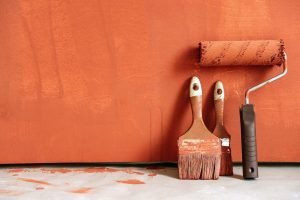 Home Close-up of paint rollers and brushes with orange paint against a painted wall.