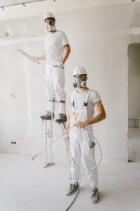 Home Two painters in protective gear working on a home renovation project, wearing masks and white uniforms.